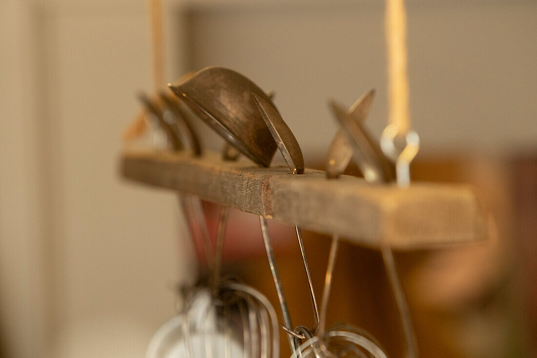 Closeup of set of hanging kitchen utensils, including spoons and a strainer, with a soft-focus background