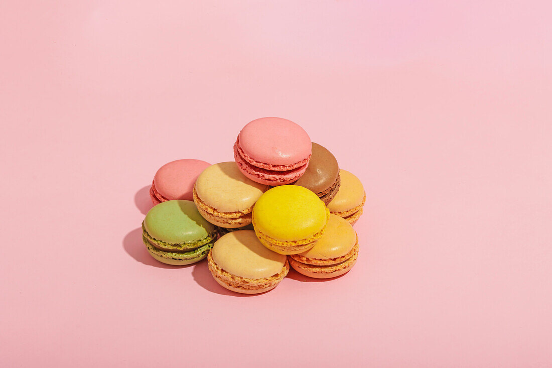 Appetizing various sweet colorful macaroons placed in heap on pink background of studio
