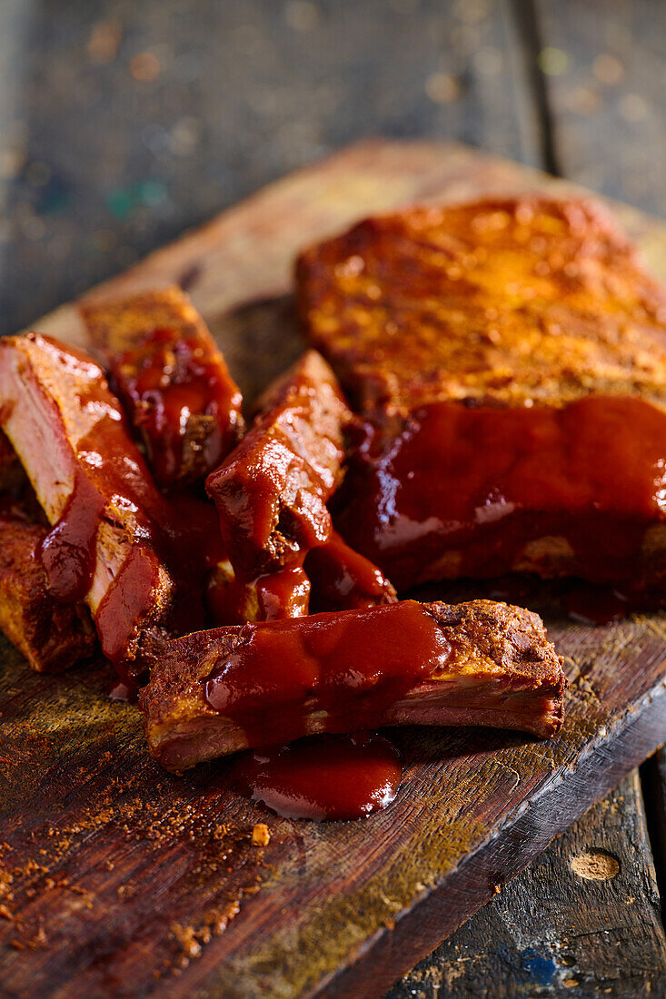 High angle of appetizing grilled pork ribs with ketchup served on wooden board in kitchen against blurred background