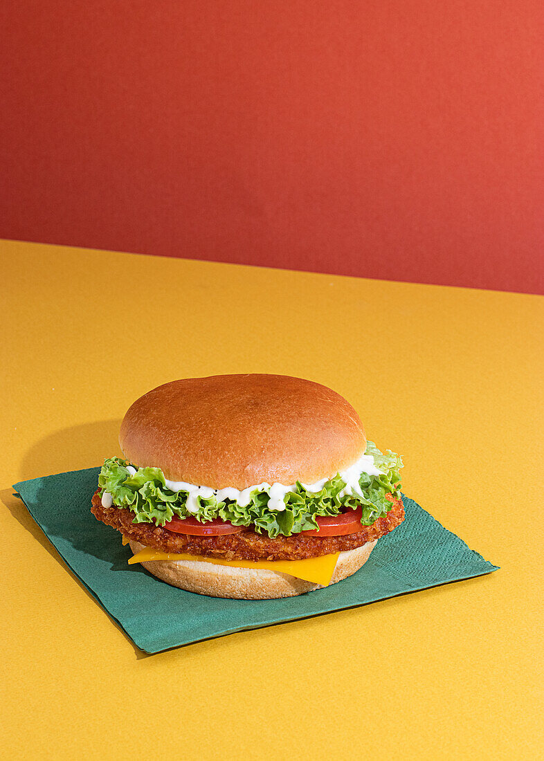 Leckerer Fisch-Burger mit Tomaten, Käsescheiben und frischem Salat auf gelbem und rotem Hintergrund