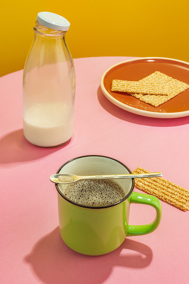Glass bottle of milk and cup of aromatic coffee on pink table against yellow background
