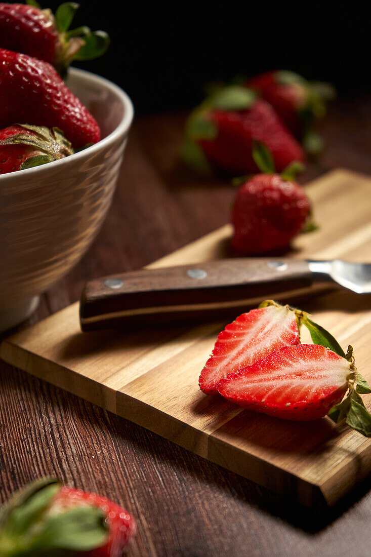 From above of fresh strawberries and knife on cutting board with cut juicy slices placed on wooden surface