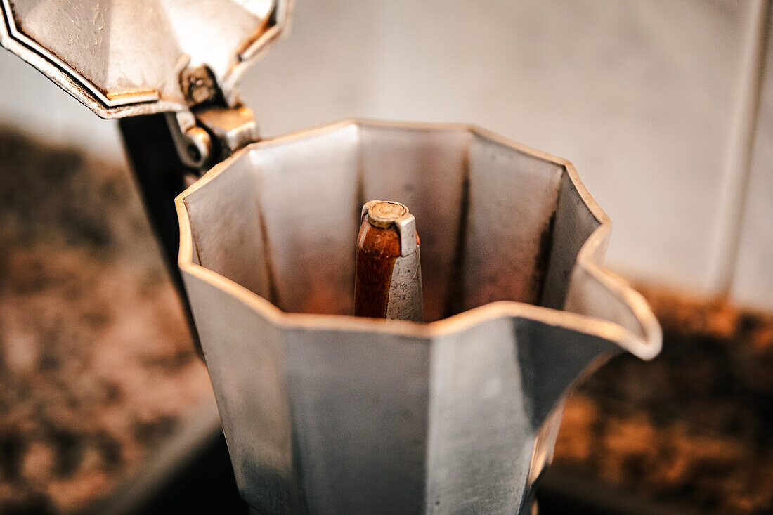 Close-up of stainless steel stovetop espresso maker placed on sleek cooktop with an ornate tiled backsplash providing a contrasting backdrop emphasizing the allure of home brewed Italian coffee