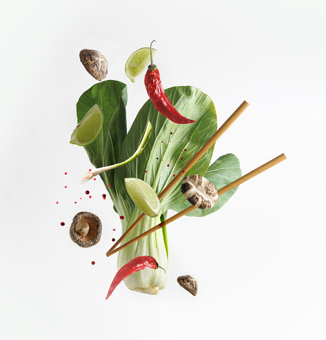 Asiatisches Essenskonzept mit fliegenden Zutaten: Bok choy, Essstäbchen, Limette, Shiitake, Gewürze und Chili auf weißem Hintergrund. Levitation Essen. Frontansicht