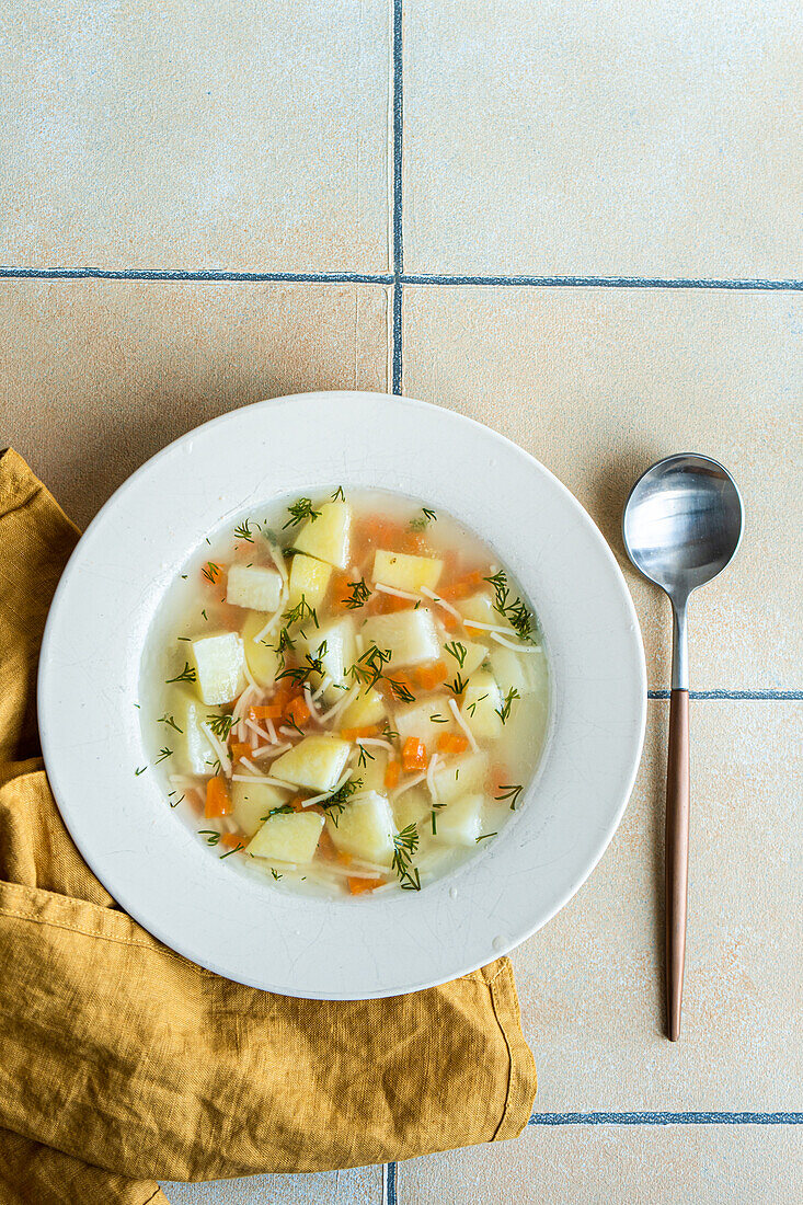 From above served healthy soup with carrot and potatoes on tiled ceramic background