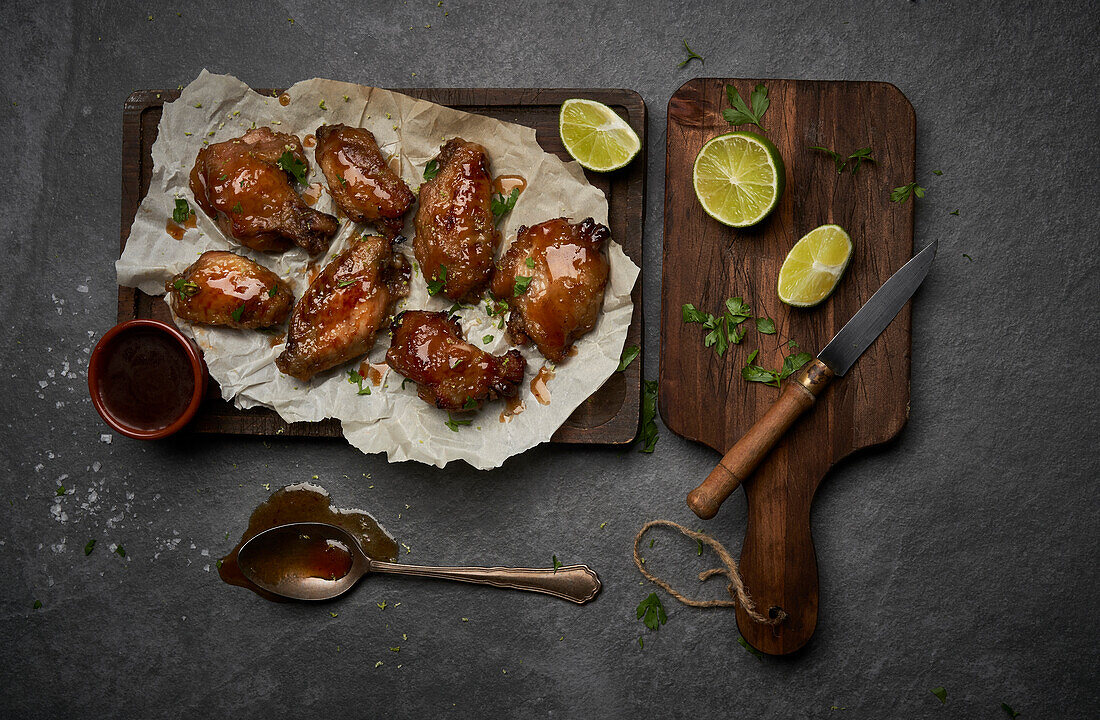From above of appetizing grilled marinated chicken wings with ginger vinegar placed on plate with sauce and served with onions on wooden cutting board with knife on gray hard surface