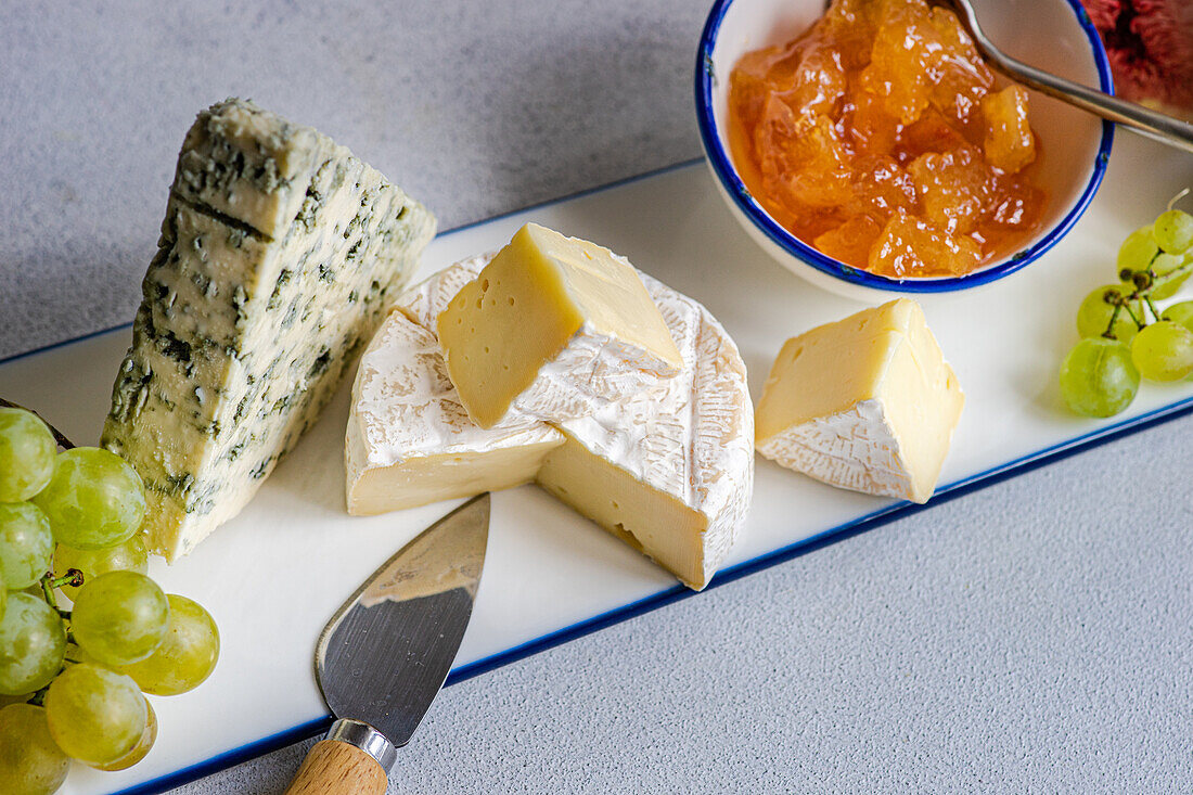 From above assorted yummy snacks with different types of cheese and sweet served on ceramics plate with grapes