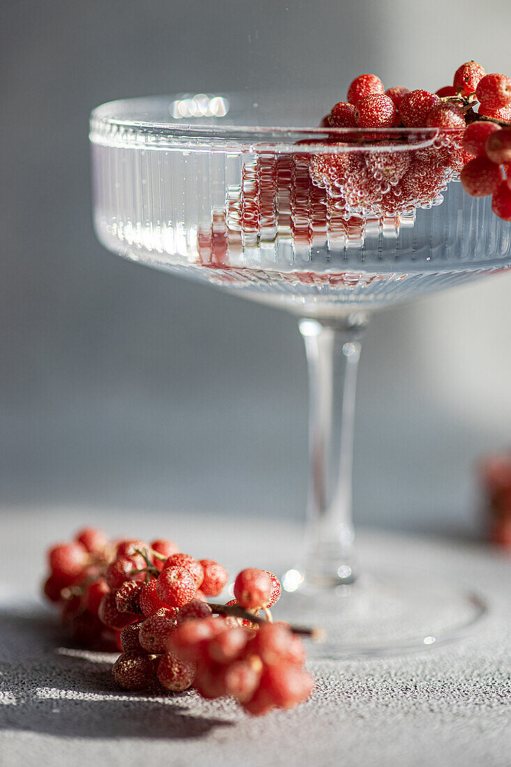 A sophisticated glass overflows with water and delicate red berries, set against a soft-light background