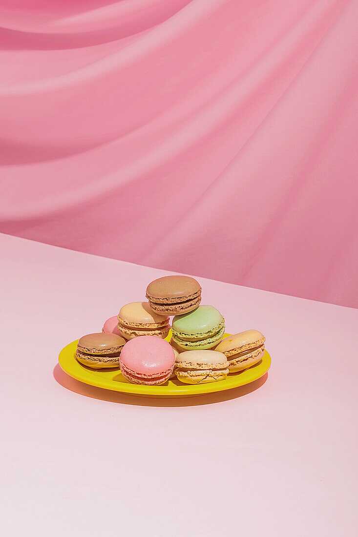 Delicious sweet multicolored macaroons placed on bright yellow round shaped plate against pink background