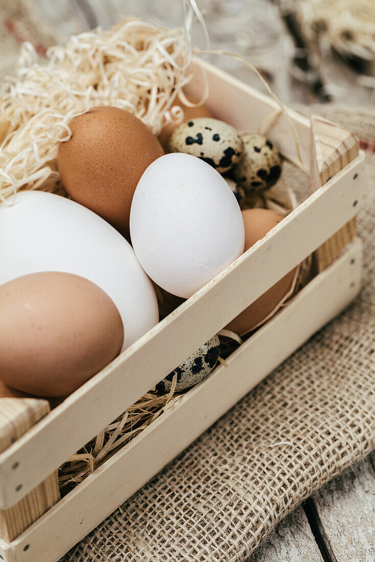 Close-up view of a wooden basket filled with brown, white, and speckled quail eggs nestled in straw.