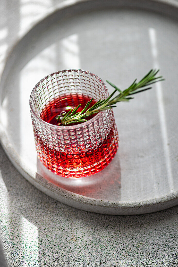 Top view of elegant cocktail with cherry and apple juice mixed with vodka garnished with a fresh rosemary sprig presented on a circular tray