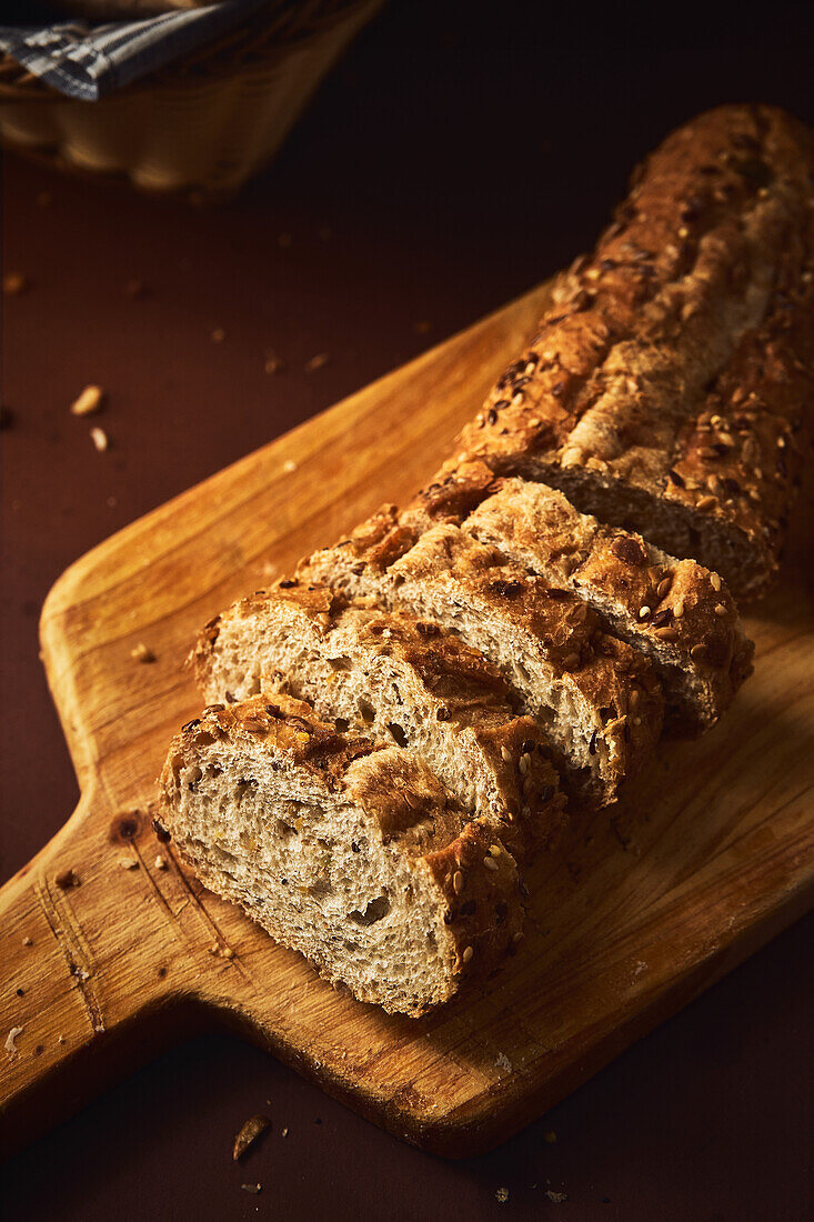 High angle of delicious freshly baked bread with crispy crust sprinkled with mix of seeds and placed on wooden cutting board