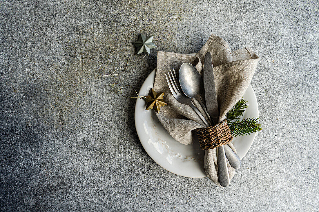 Blick von oben auf Vintage-Besteck mit Serviette Löffel Messer und Gabel auf einem Teller auf grauer Oberfläche in der Nähe von Weihnachtsschmuck im Tageslicht platziert