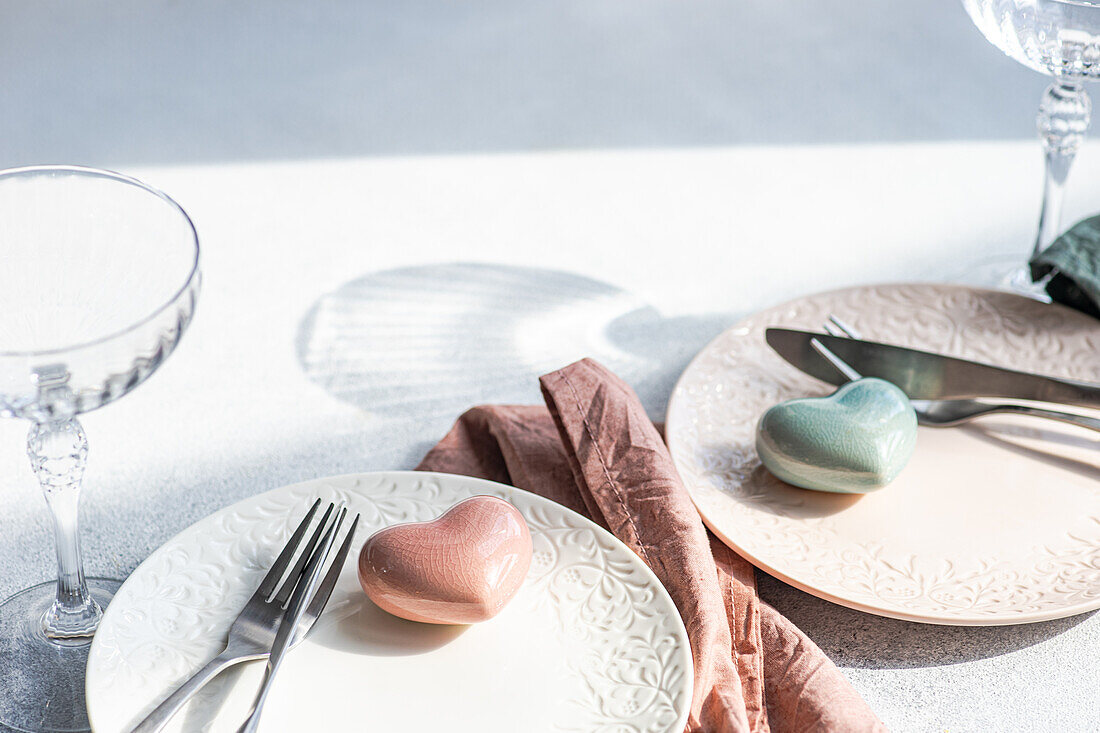 Top view of ceramic plate with cutlery and napkin with heart shaped decor crystal placed on concrete surface at kitchen table for meal during Valentine's day celebration