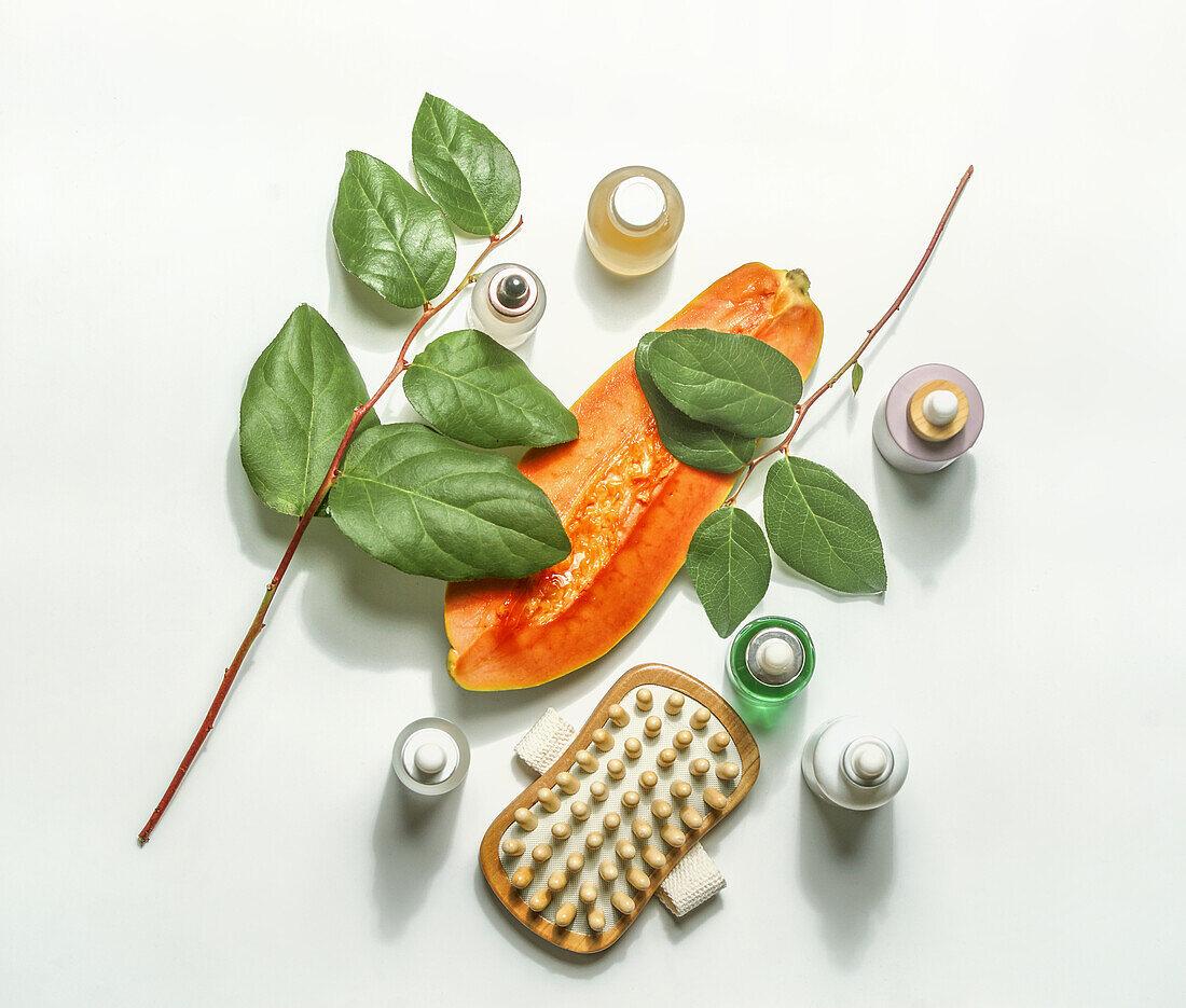 Body care cosmetic setting with halved papaya, beauty products, dry massage brush and green leaves on white background. Sustainable beauty skin care concept. Top view.