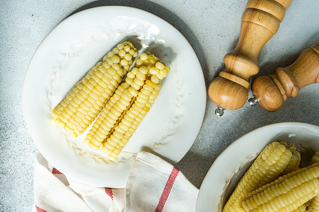 Top view of ripe sweet corns served on plates near napkin on gray table