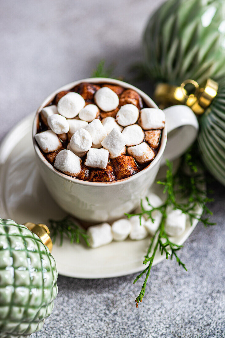 Draufsicht auf leckeren Kakao mit Marshmallow auf einem Teller mit Tannenzweigen in der Nähe von Weihnachtskugeln