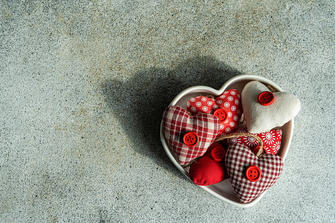 From above heart shaped bowl filled with assorted handmade fabric hearts on a textured concrete background during Valentine's day celebrations
