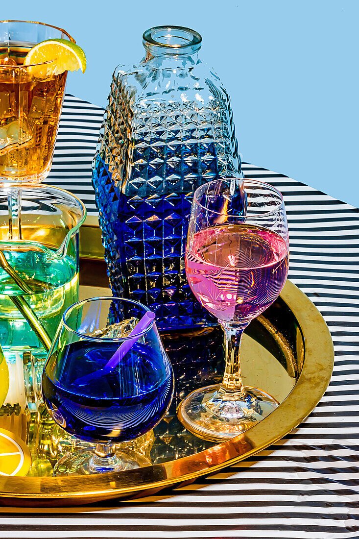 From above different varieties of cocktails comprising blue margarita Long Iceland iced tea wine daiquiri in attractive glasses and jar placed on plate on striped cloth against blue background