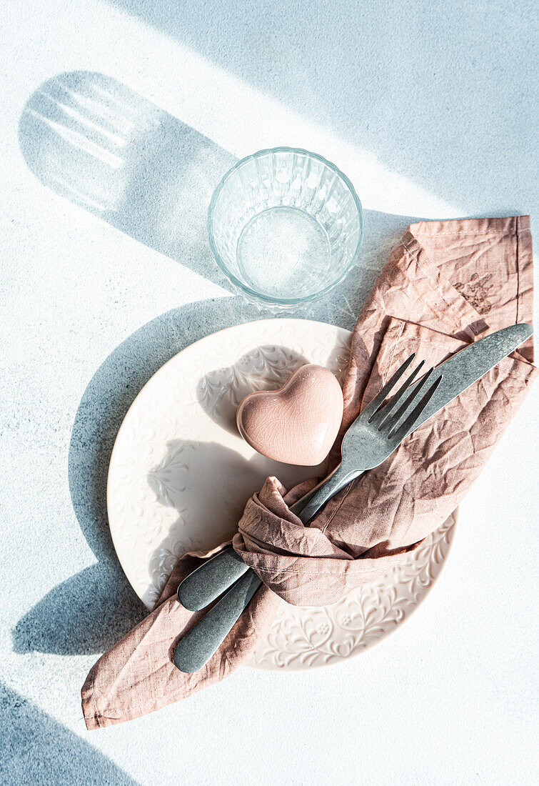 Draufsicht auf einen Keramikteller mit Besteck und Serviette mit herzförmigem Kristalldekor auf einer Betonfläche am Küchentisch für eine Mahlzeit während der Valentinstagsfeier