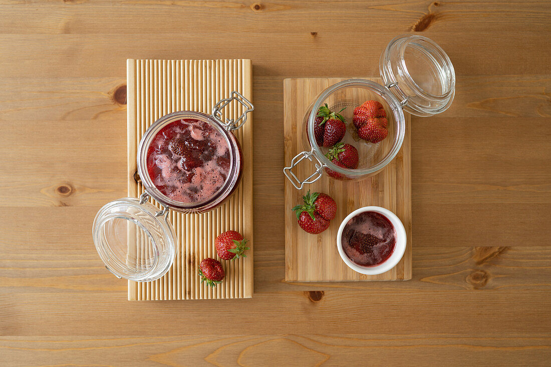 Blick von oben auf ein Glasgefäß mit frischen Erdbeeren und Früchten auf einem Holzbrett über einem Tisch bei Tageslicht