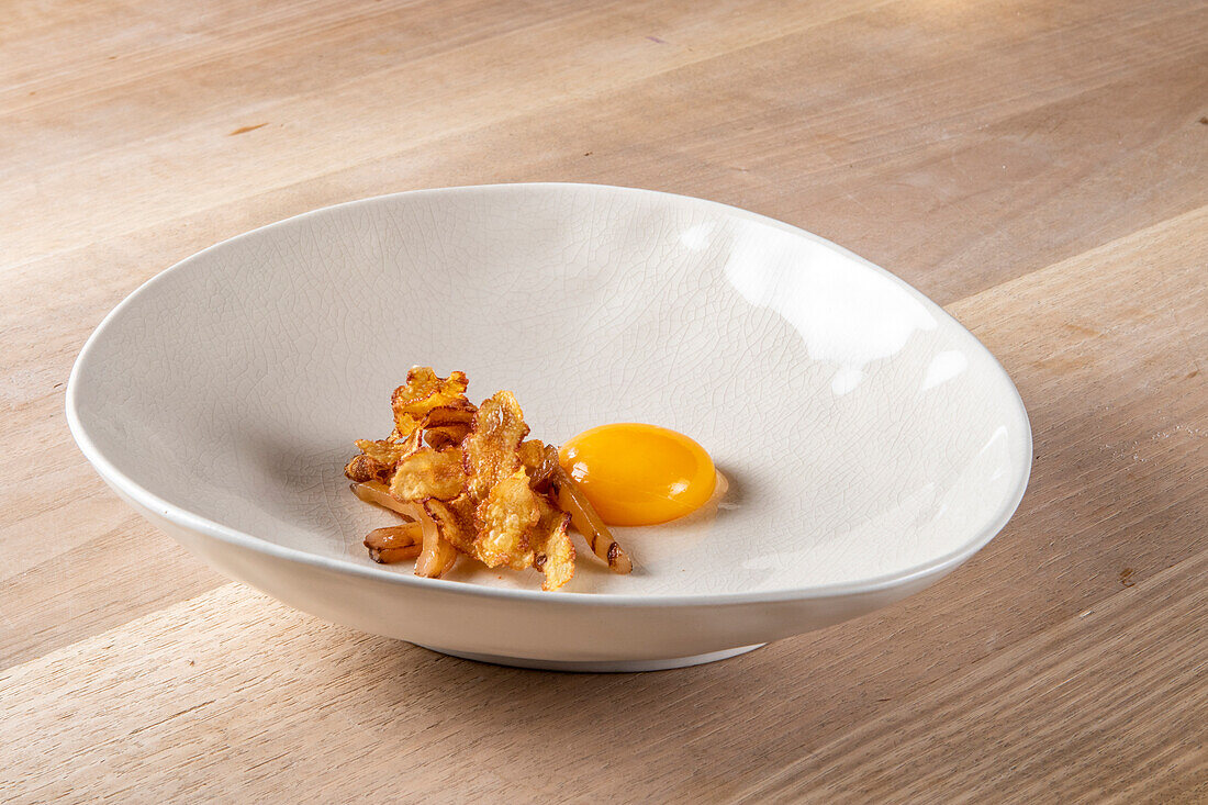 Closeup of fried strips with raw egg yolk in plate on wooden table