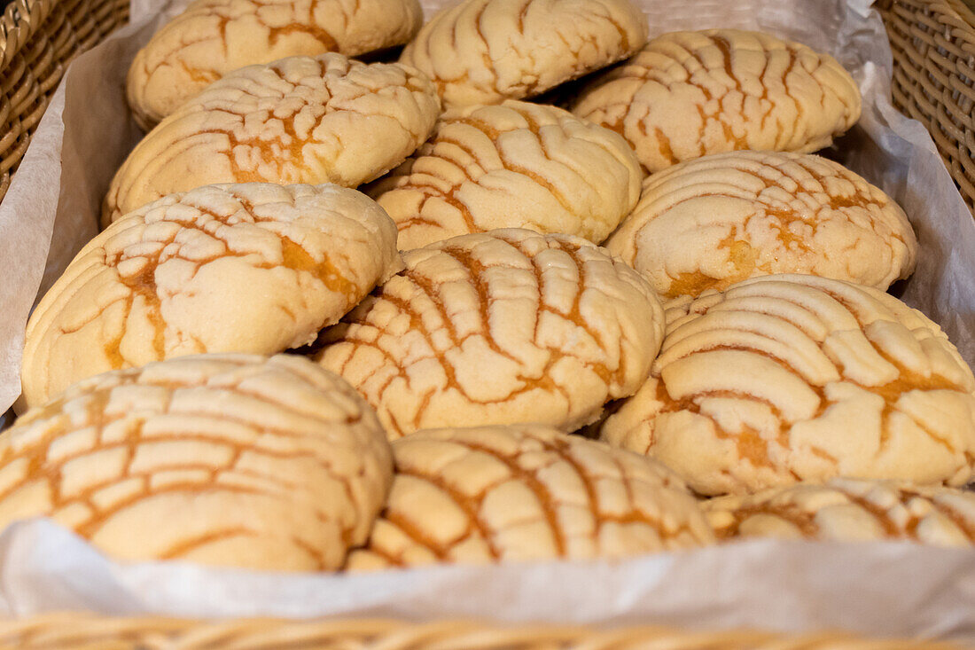 Nahaufnahme von frisch gebackenen, leckeren, knusprigen Concha-Broten, die in einem schwächeren Korb in Papier eingelegt sind