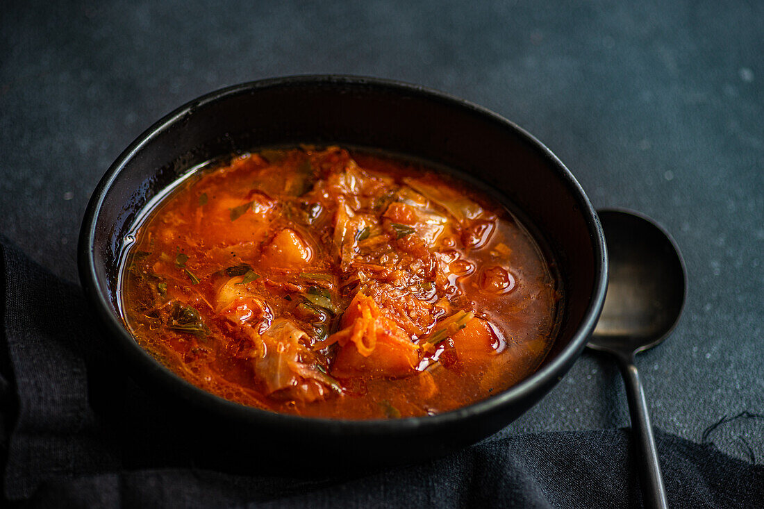 Blick von oben auf eine traditionelle ukrainische Rote-Bete-Suppe, bekannt als Borschtsch ohne Fleisch, serviert auf einem schwarzen Teller mit Löffel vor dunkler Oberfläche