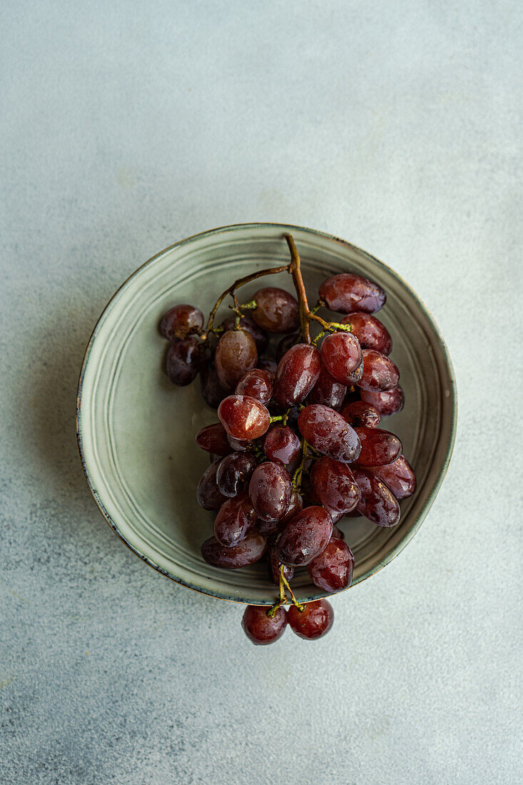 Top view of red Champagne grape variety served on dark plate against gray background in daylight