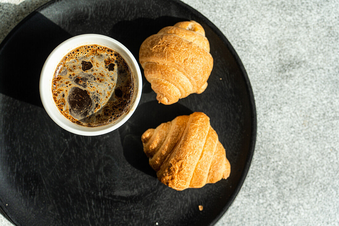 Draufsicht auf einen schwarzen Kaffee und frisch gebackene Croissants auf einem Betontisch