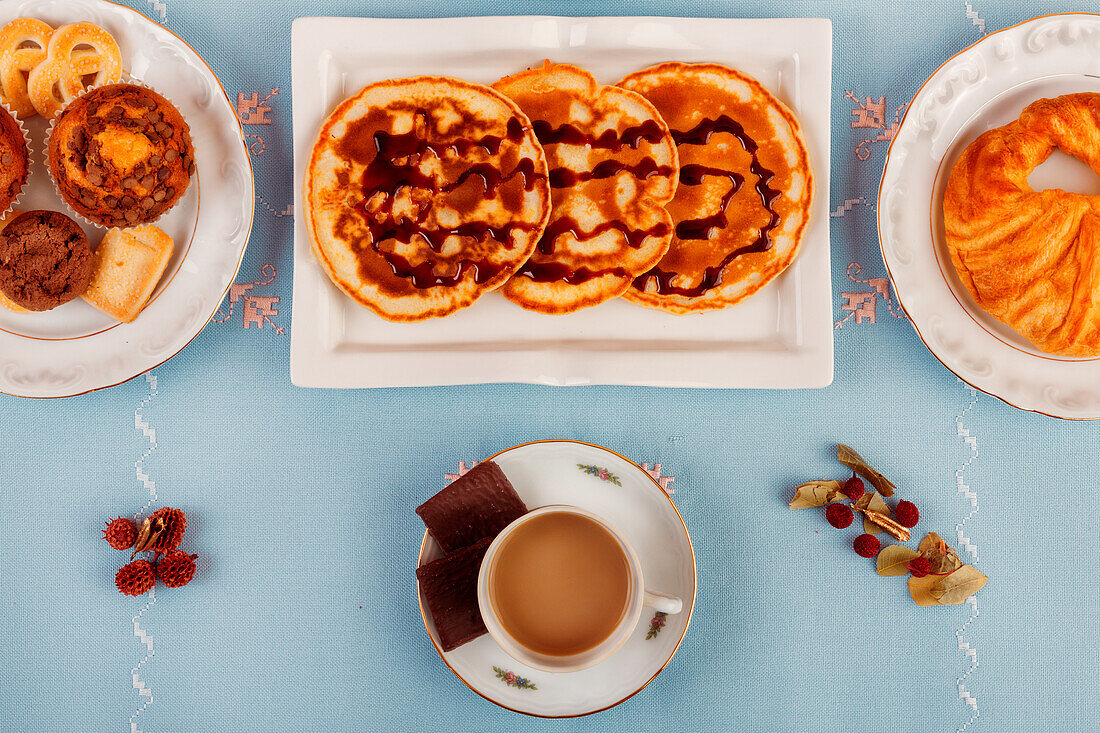 A top-view of a continental breakfast setup featuring pastries, cereal, fresh fruit, and beverages, laid out on a blue surface.