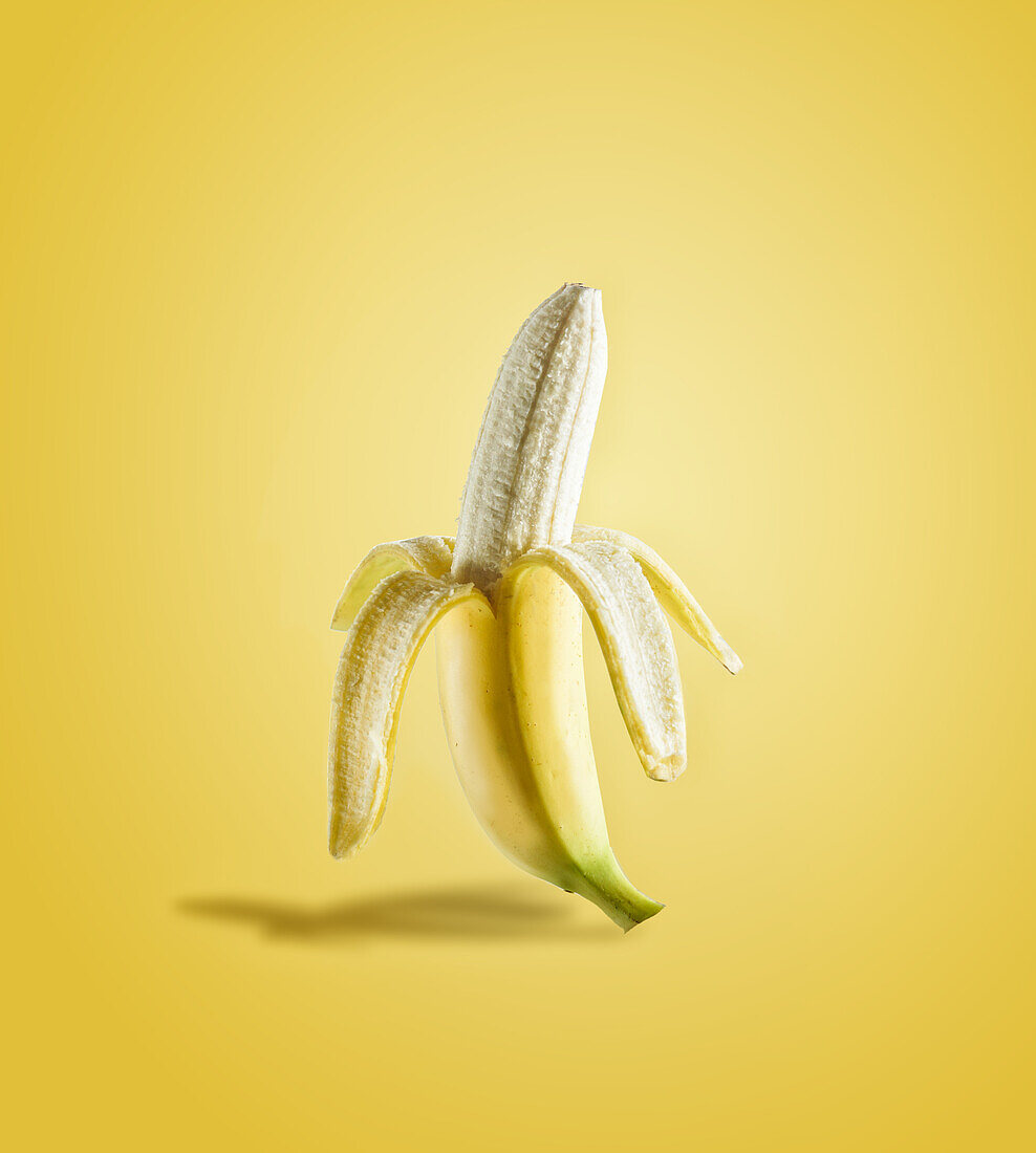 Half peeled banana in sunlight on yellow background. Delicious tropical fruit. Front view.