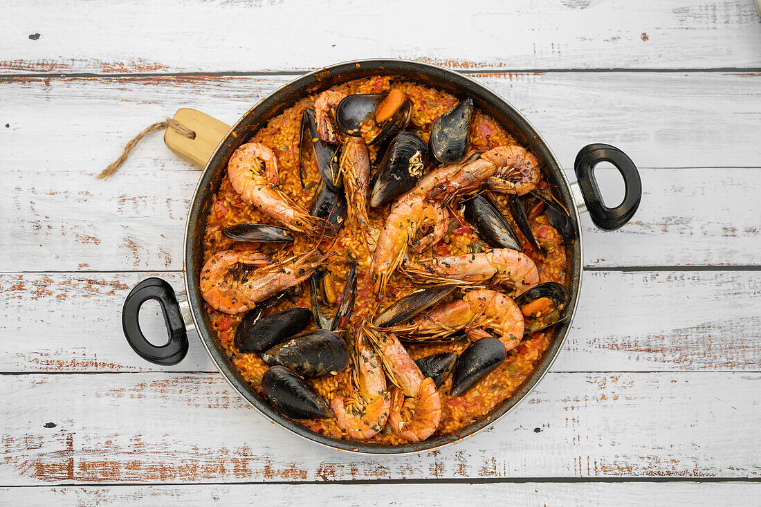 Draufsicht auf eine frisch gekochte spanische Paella mit Reis und Meeresfrüchten in einer Pfanne auf einem Holztisch in der Küche