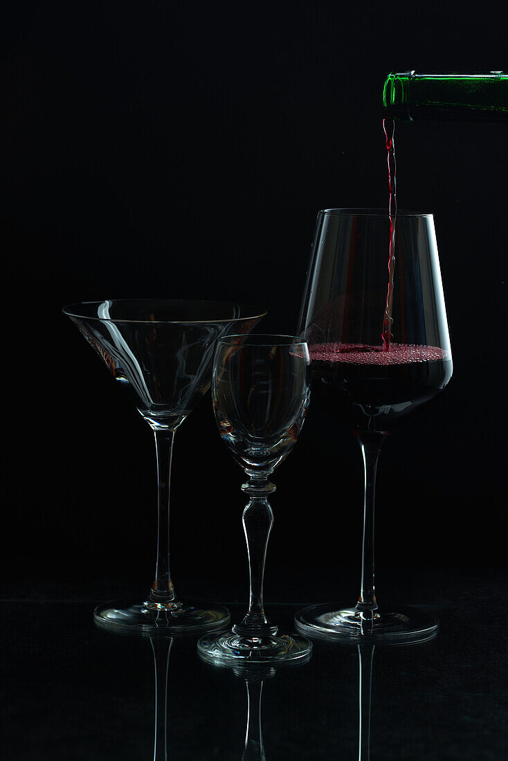 Eleganter Rotwein fließt in ein Glas inmitten von leeren Stielgläsern vor einem dunklen Hintergrund