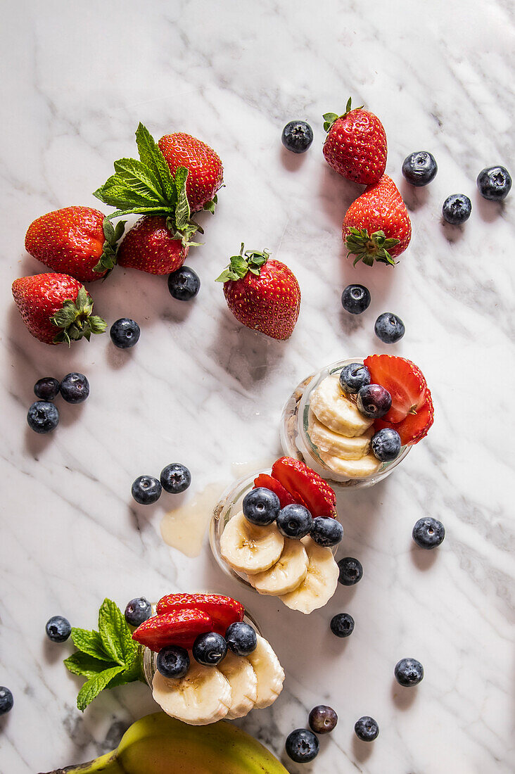Frische Erdbeeren und Blaubeeren mit in Scheiben geschnittener Banane in Tassen und auf weißem Marmortisch in einem hellen Raum