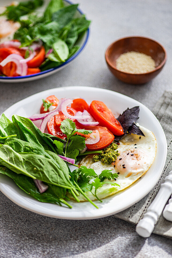 Frischer Keto-freundlicher Frühstücksteller mit Eiern, Spinat, Tomaten und anderem Gemüse auf einem strukturierten Hintergrund