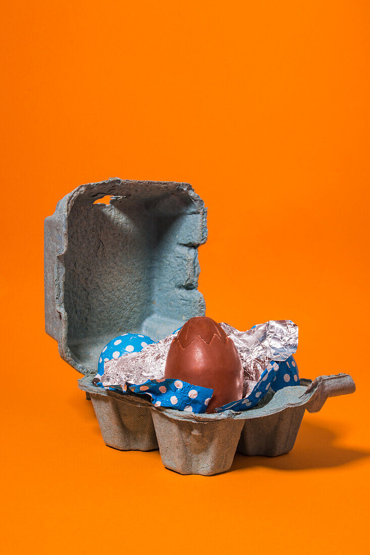Close-up of some blue and red easter eggs inside a gray cardboard box on an orange background