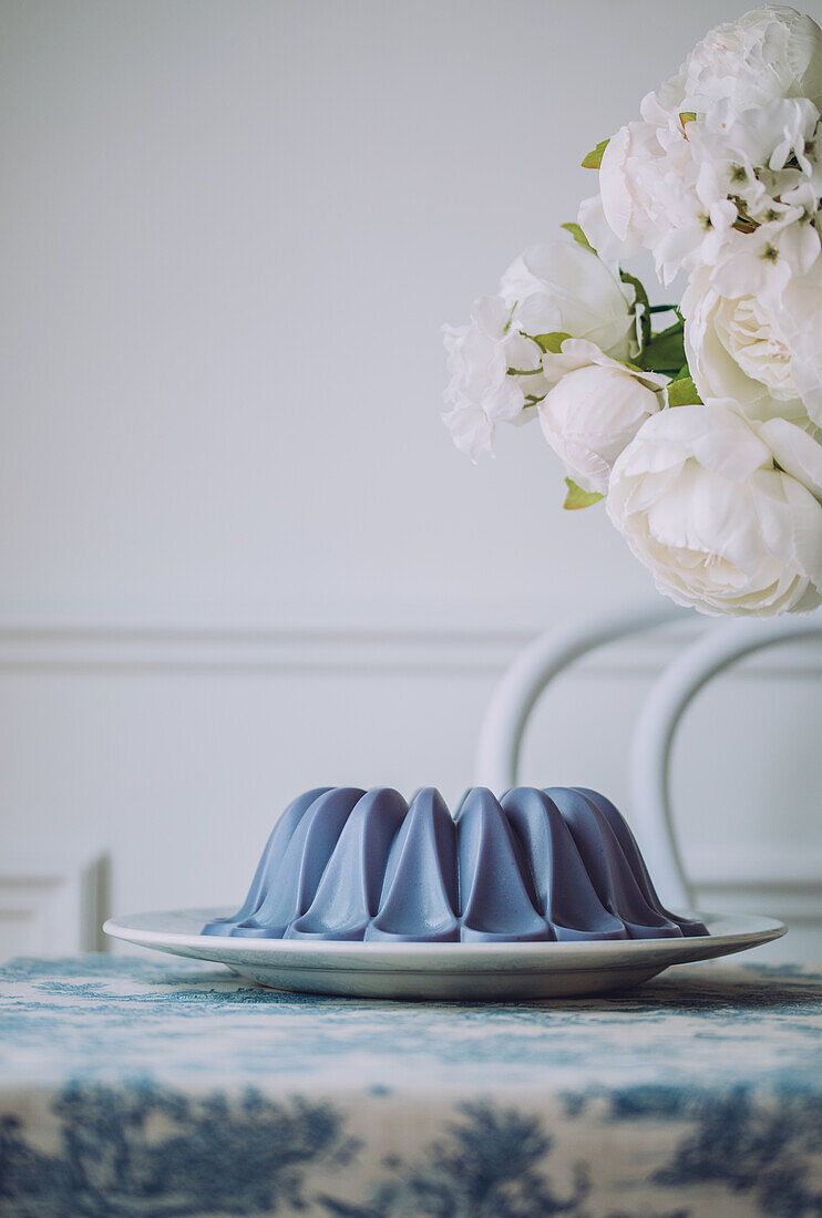 Süßes veganes blaues Panna-Cotta-Dessert auf einem Teller, der auf dem Tisch neben Blumen steht