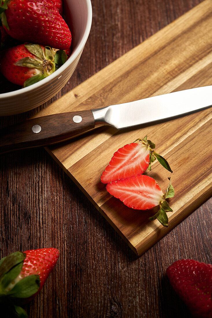 From above of fresh strawberries and knife on cutting board with cut juicy slices placed on wooden surface