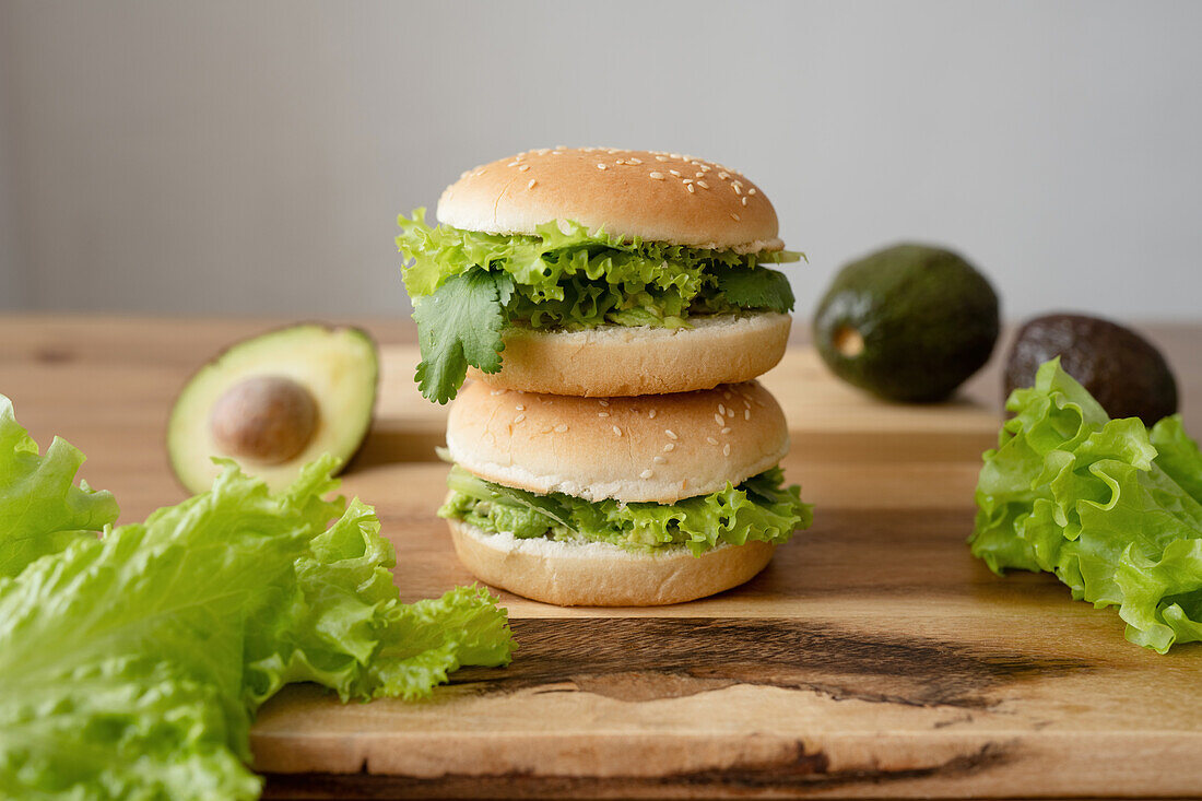 Tasty vegetarian burgers with fresh lettuce and avocado on wooden cutting board against gray background