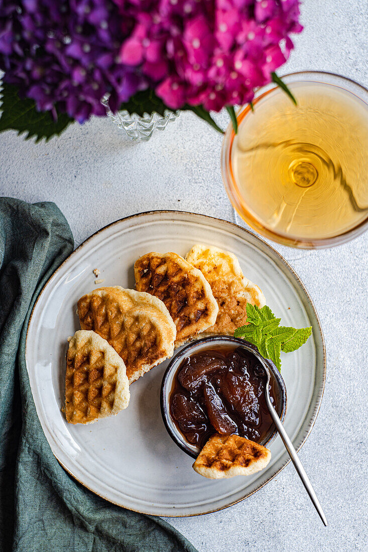 Top view of appetizing sweet waffles served with peach jam on round table near glass with drink in garden with blooming purple Hydrangea flowers