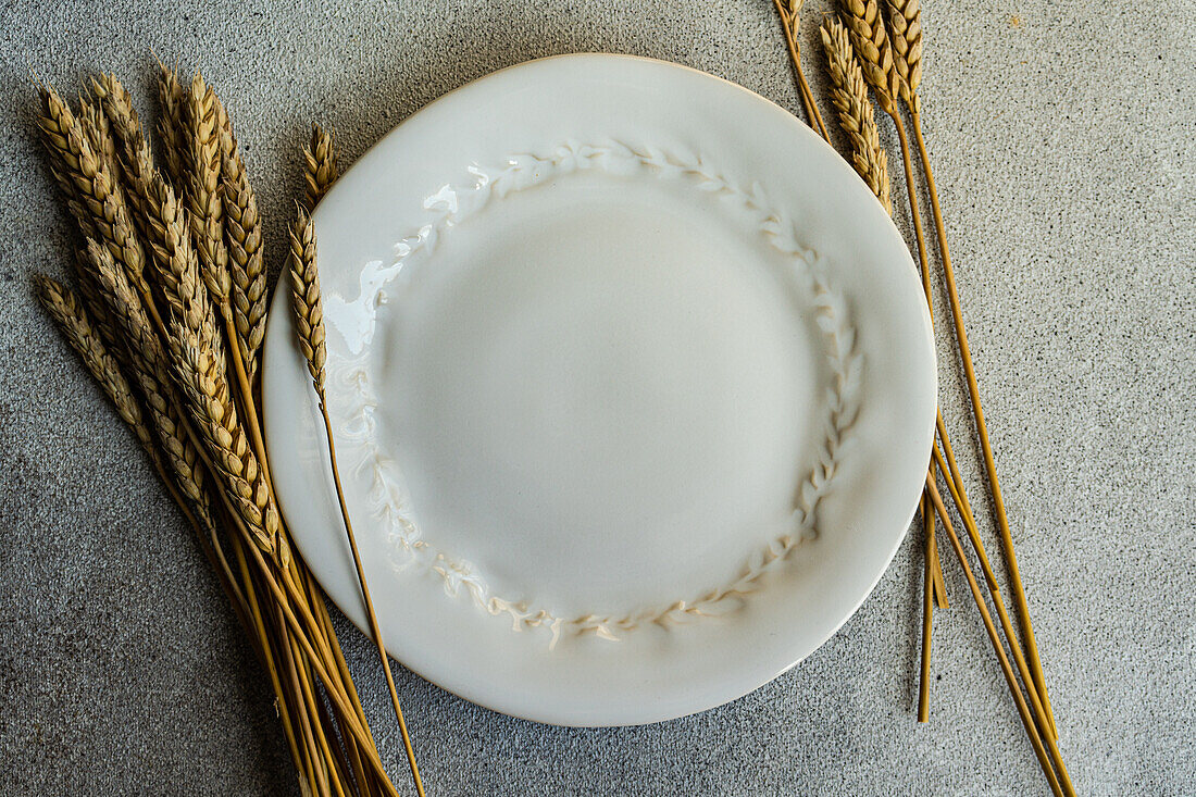 Draufsicht auf einen Strauß Weizenähren, der zwischen Tellern auf einem grauen Tisch liegt