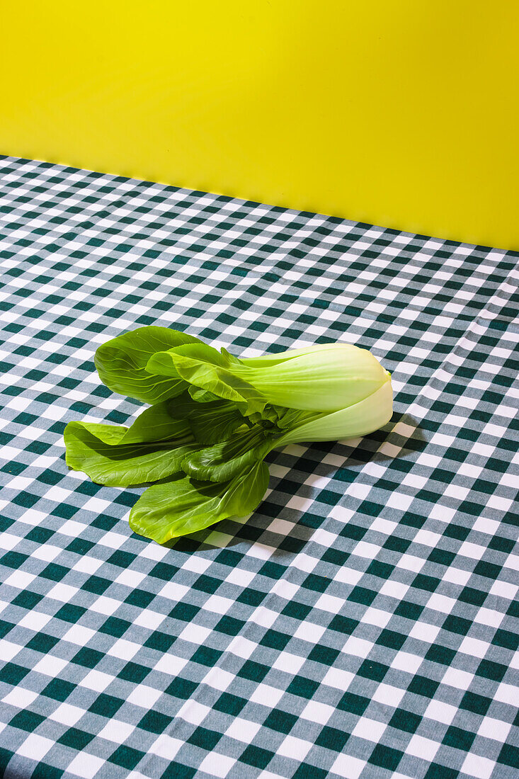 Frischer grüner Bok Choy-Kohl auf kariertem Tischtuch vor gelbem Hintergrund