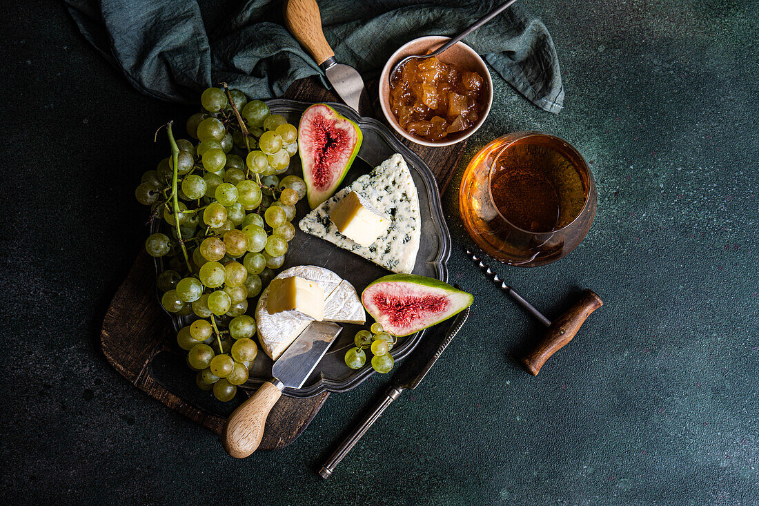 Draufsicht auf verschiedene leckere Snacks mit Käse und serviert auf einem Teller, der auf einem Holzbrett mit Trauben, Feigen und Marmelade steht