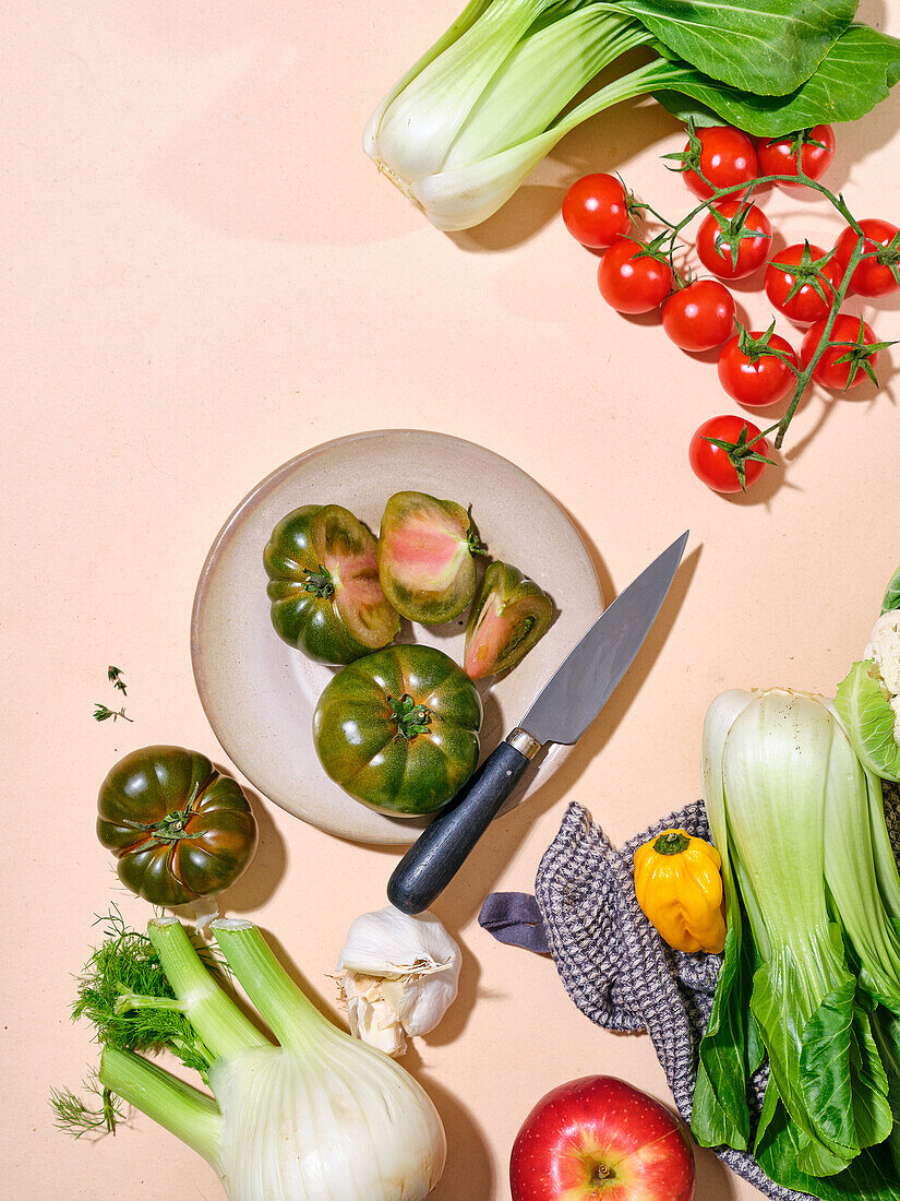 Grüne Tomaten mit anderem Gemüse wie Bok Choy in hellem Sonnenlicht flachgelegter Teller mit Messer mit Kopierraum auf beigem Hintergrund
