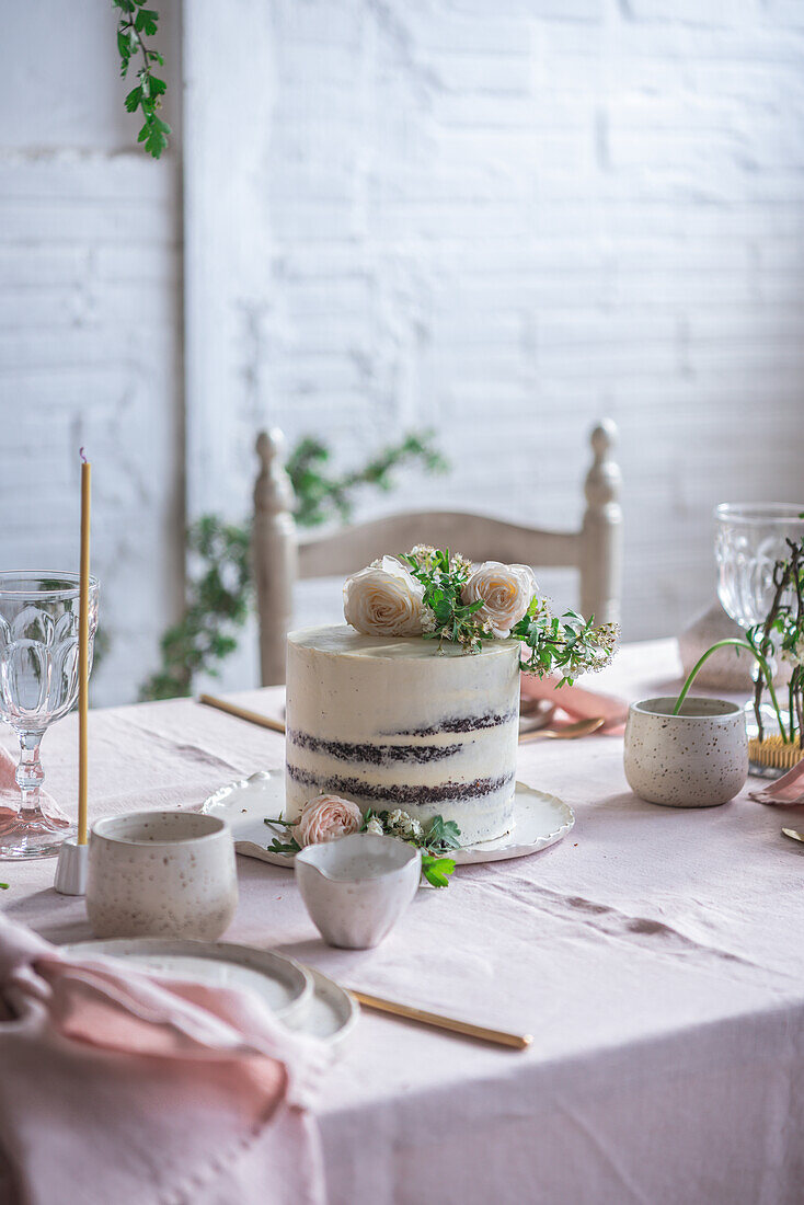 Eleganter Tisch mit Tellern und Blumen in der Nähe eines leckeren Kuchens auf einem rosa Tischtuch vor einer Backsteinwand