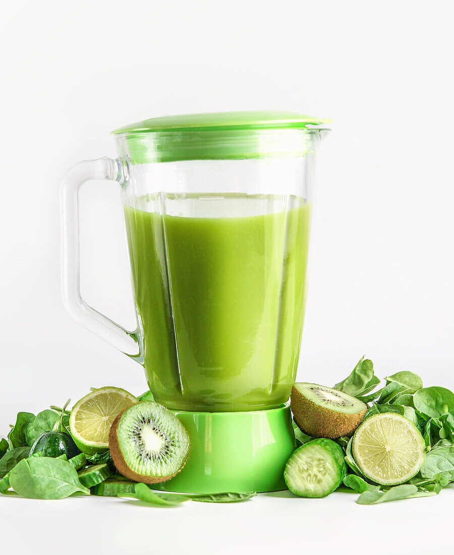 Mixer mit grünem Smoothie mit Zutaten: Kiwi, Gurke, Limette und Spinat auf weißem Hintergrund. Zubereitung von gesundem Saft. Vorderansicht