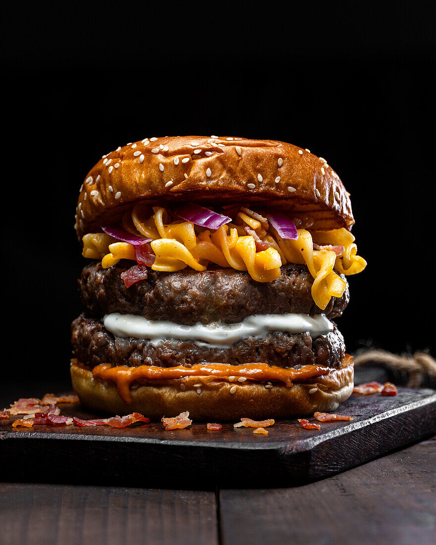 Closeup of hamburger with macaroni and cheese placed on wooden tray on table against dark background