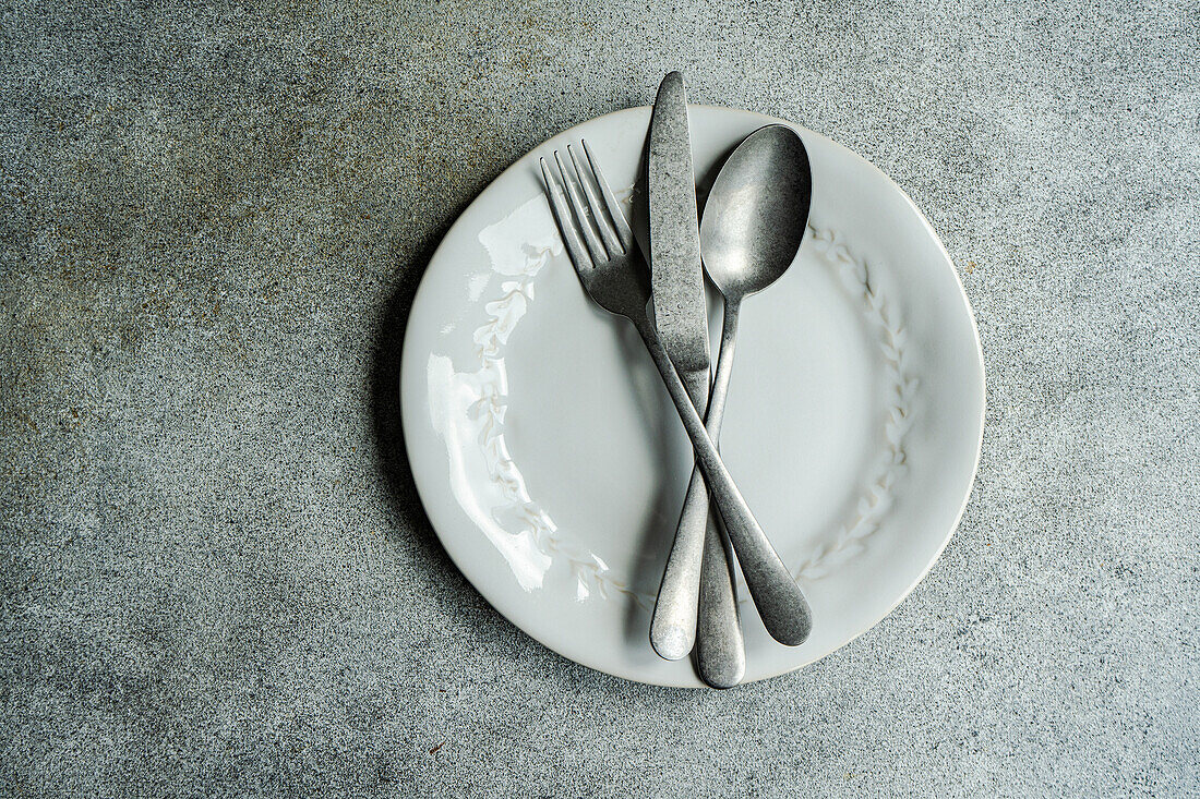 Top view of vintage cutlery set placed on white plate against gray surface in light kitchen