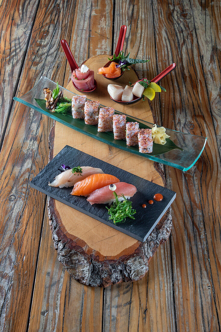 From above of delicious uramaki sushi and nigiri sushi together with sashimi in small bowls on wooden background